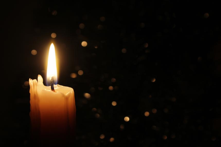 Weiße Kerzen brennen im Dunkeln, wobei der Fokus auf einer einzelnen Kerze im Vordergrund liegt.